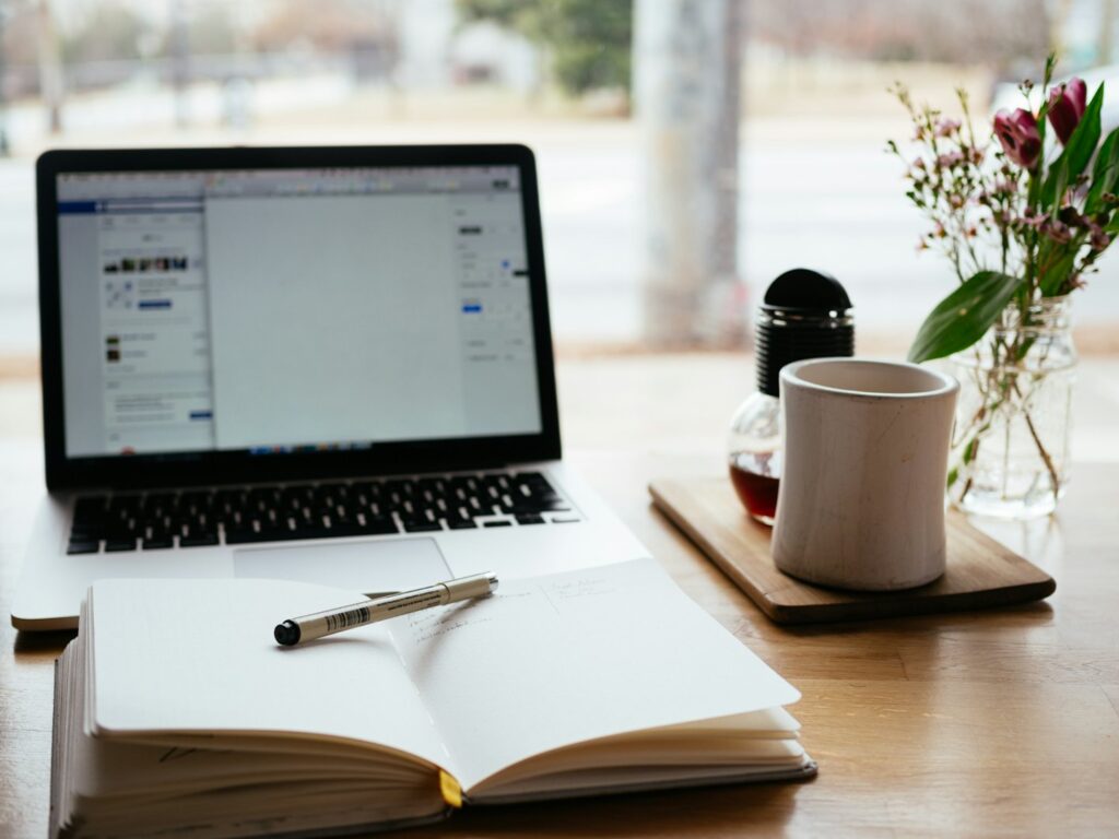 Laptop on a table with notepad and pen and cup of coffee