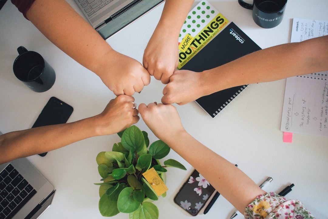 5 hands together over a desk to signify teamwork