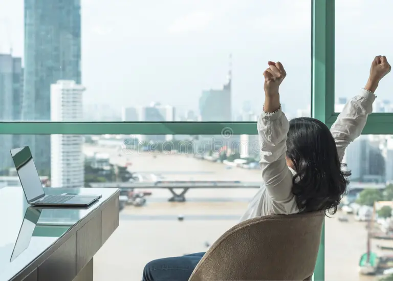 Lady sat in chair at office desk throwing her arms in the air in celebration